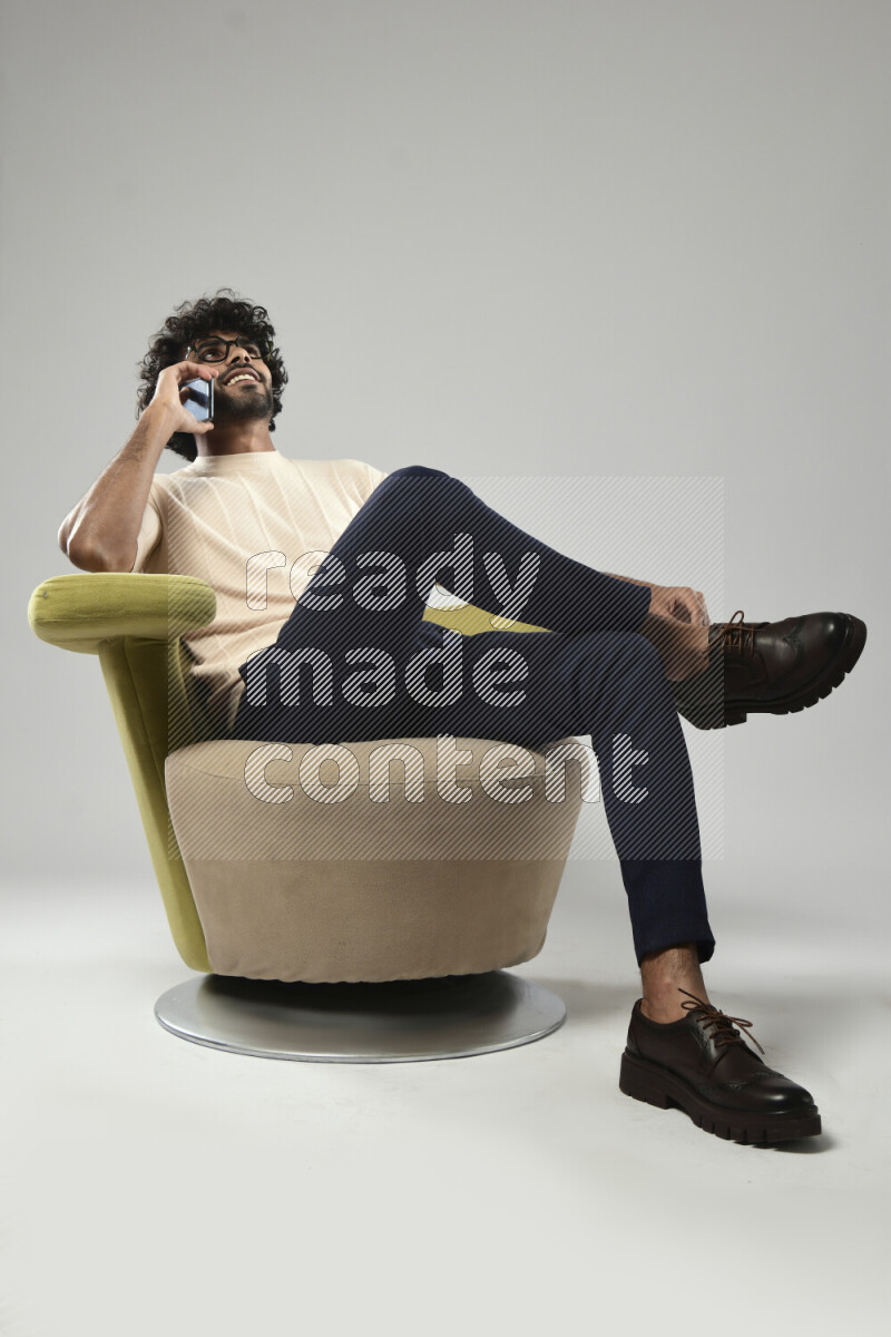 A man wearing casual sitting on a chair talking on the phone on white background