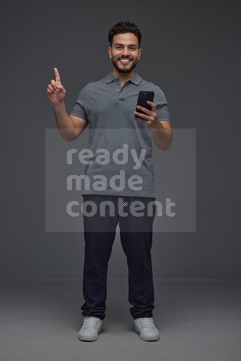 A man wearing casual standing and using his phone and making multi hand gestures eye level on a gray background