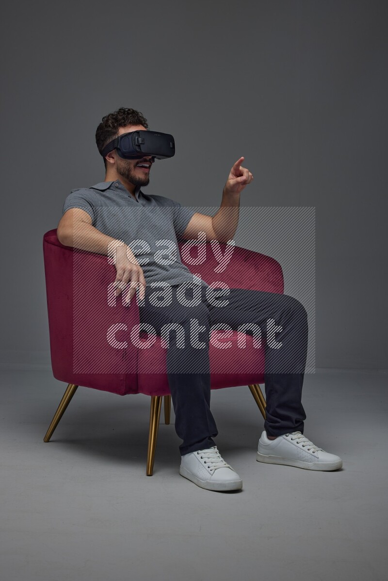 A man wearing casual and wearing VR while sitting on a burgundy chair eye level on a gray background