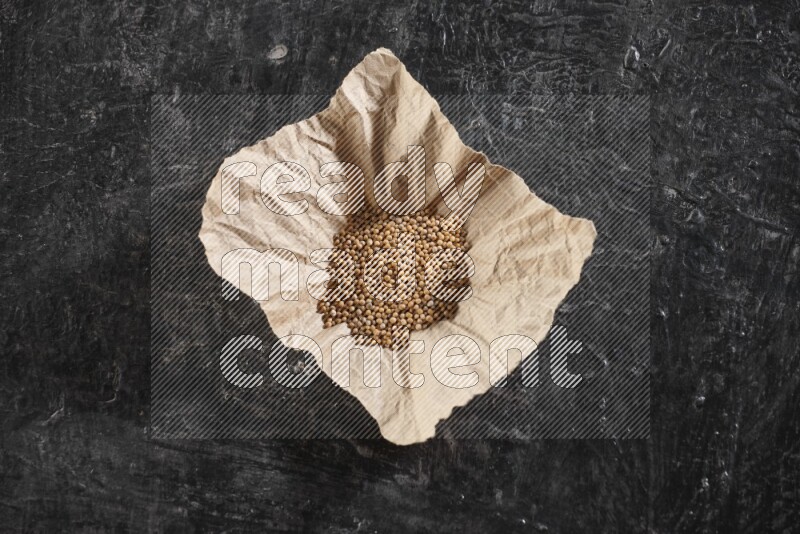 A crumpled piece of paper full of mustard seeds on a textured black flooring