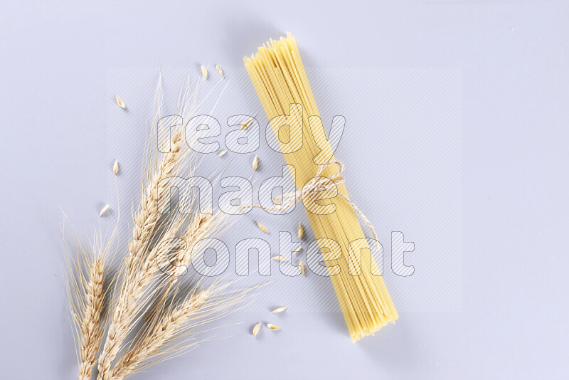 Raw pasta with wheat stalks on light blue background