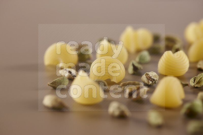 Raw pasta with different ingredients such as cherry tomatoes, garlic, onions, red chilis, black pepper, white pepper, bay laurel leaves, rosemary and cardamom on beige background