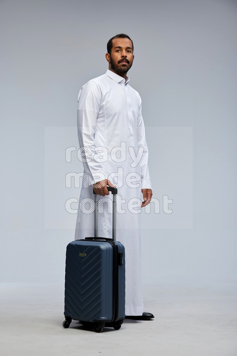 Saudi man wearing thob standing holding Travel bag on Gray background