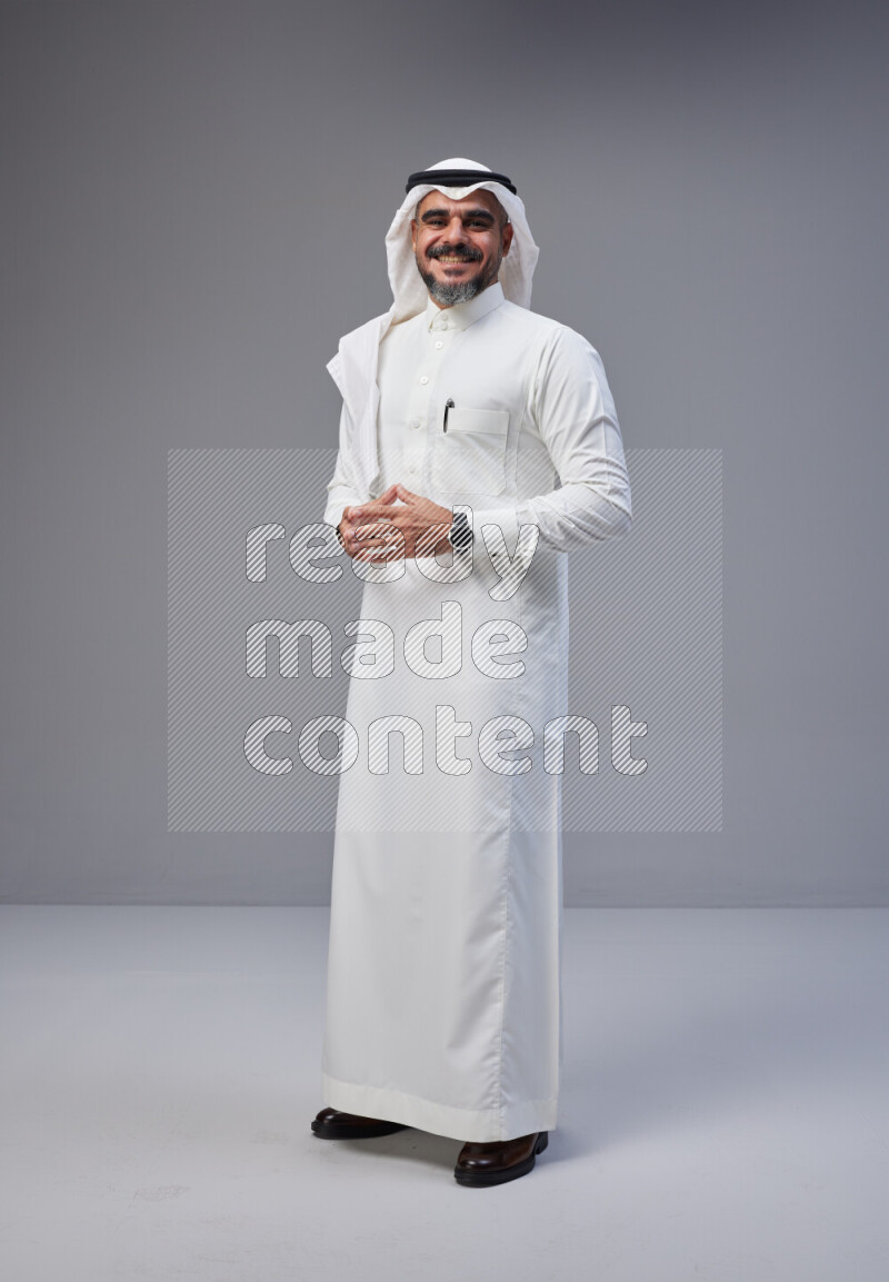 Saudi man Wearing Thob and white Shomag standing interacting with the camera on Gray background