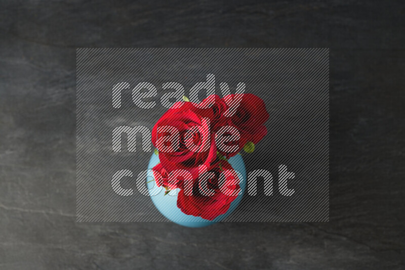 مجموعة من الورود الحمراء الزاهية في مزهرية زرقاء على خلفية من الرخام الأسود