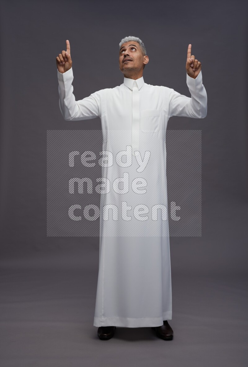 Saudi man wearing thob standing interacting with the camera on gray background