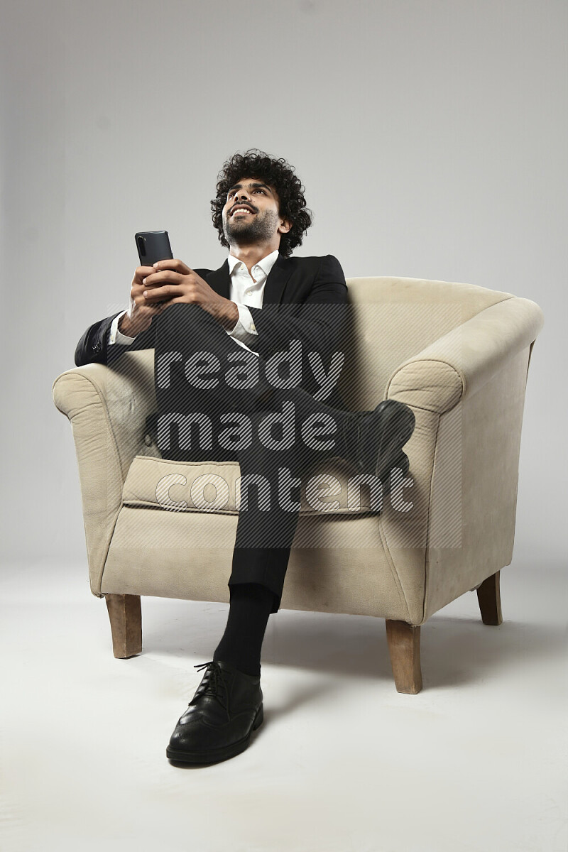 A man wearing formal sitting on a chair texting on the phone on white background