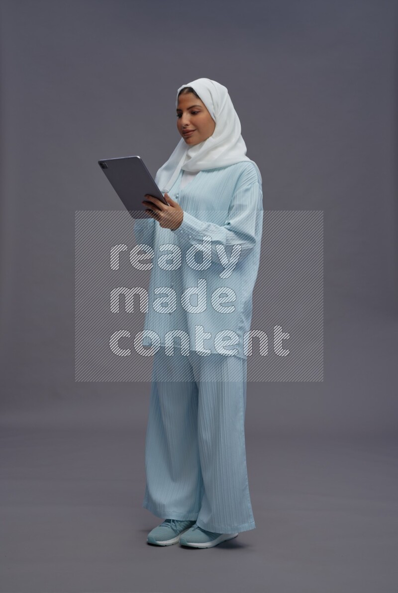 Saudi woman wearing hijab clothes standing working on tablet on gray background