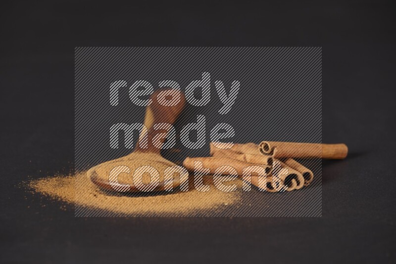 Cinnamon powder in a wooden ladle spoon with cinnamon sticks on black background