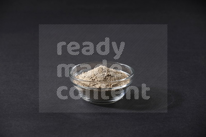 A glass bowl full of garlic powder on a black flooring