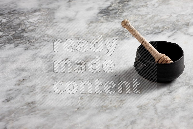 Black Pottery bowl with wooden honey handle in it, on grey marble flooring, 45 degree angle