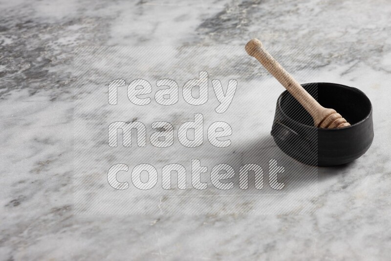Black pottery bowl with wooden honey dipper in it on grey marble background