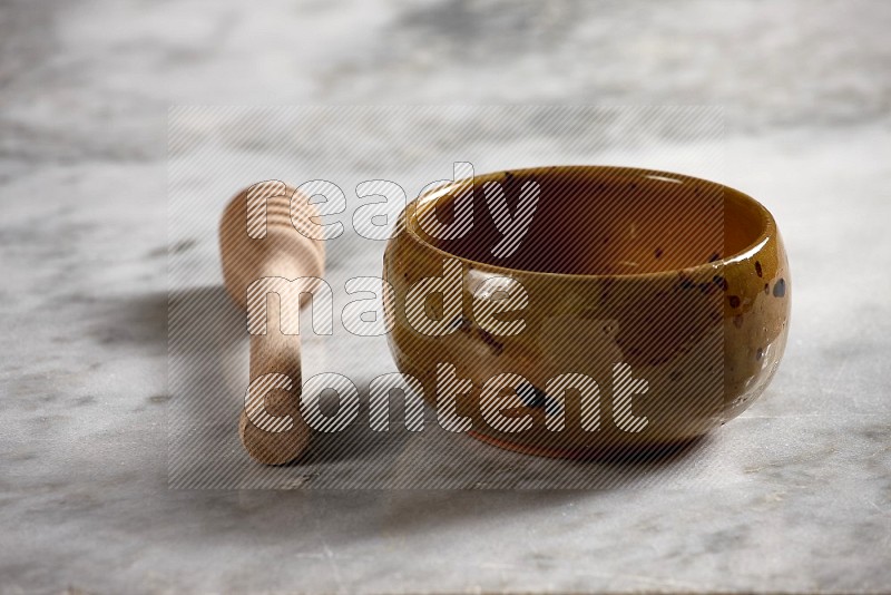 Multicolored Pottery bowl with wooden honey handle on the side with grey marble flooring, 15 degree angle