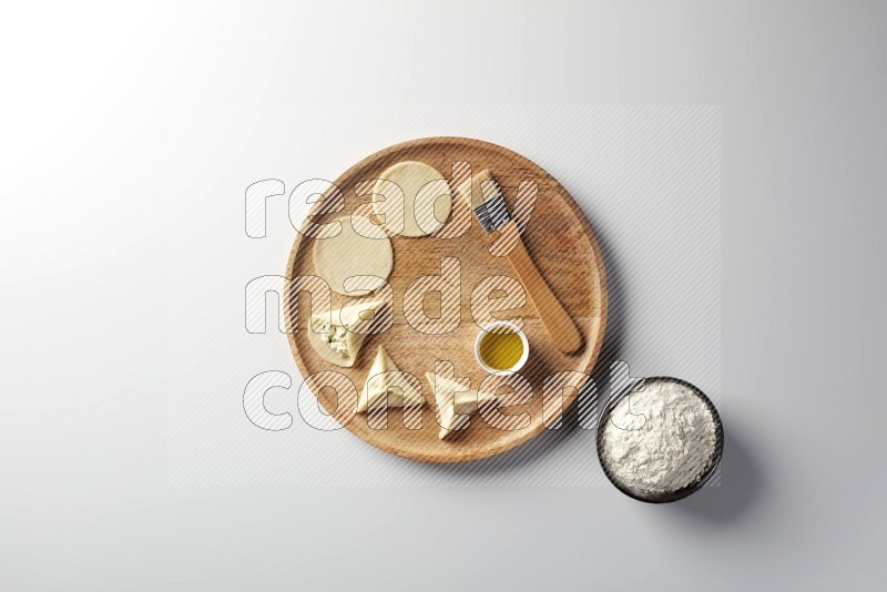 two closed sambosas and one open sambosa filled with cheese while flour, and oil with oil brush aside in a wooden dish on a white background