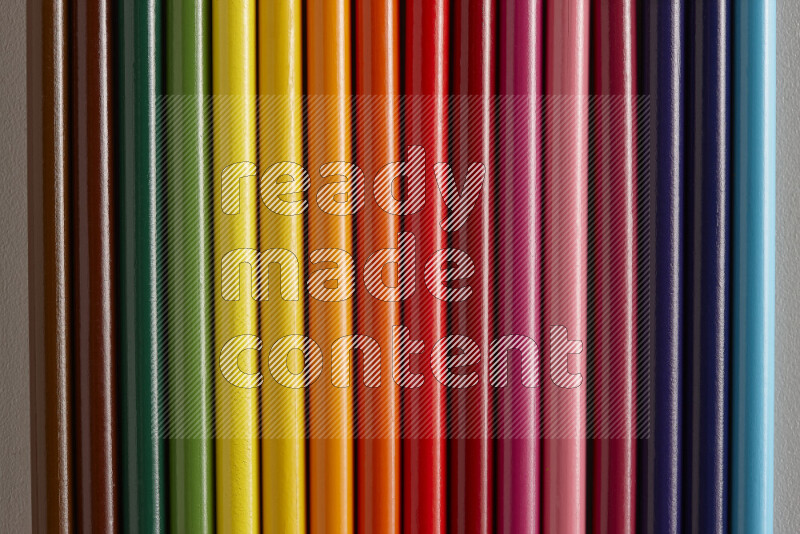 A collection of colored pencils arranged showcasing a gradient of different hues on grey background