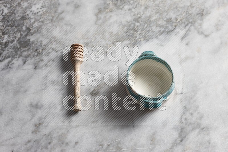Multicolored pottery bowl with wooden honey dipper on the side on grey marble background