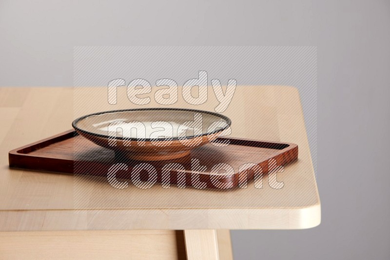 multi-colored pottery Plate placed on a rectangular wooden tray on the edge of wooden table