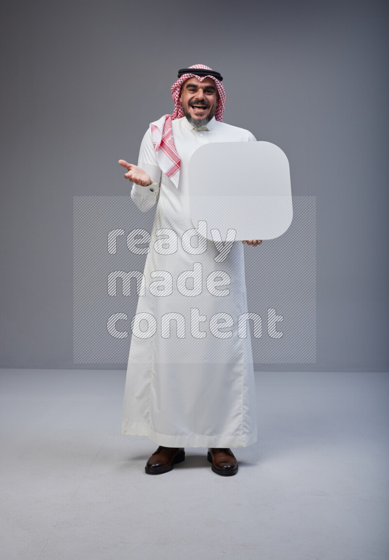 Saudi man Wearing Thob and red Shomag standing holding social media sign on Gray background