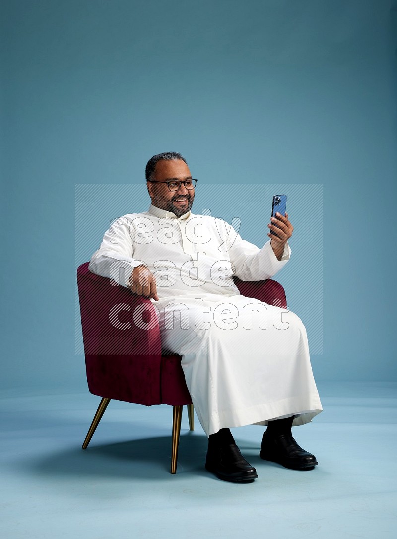 Saudi Man without shimag sitting on chair taking selfie on blue background