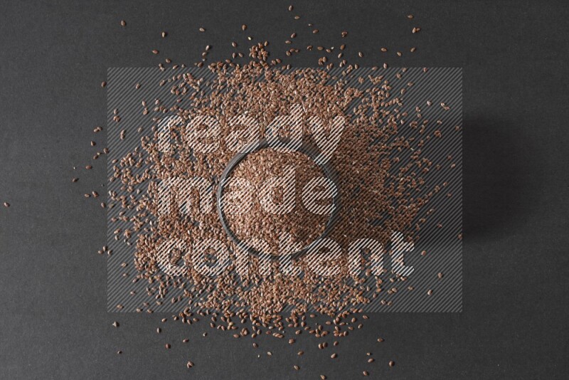 وعاء فخاري أسود ممتلئ بحبوب بذر الكتان محاط بالبذور على أرضية سوداء