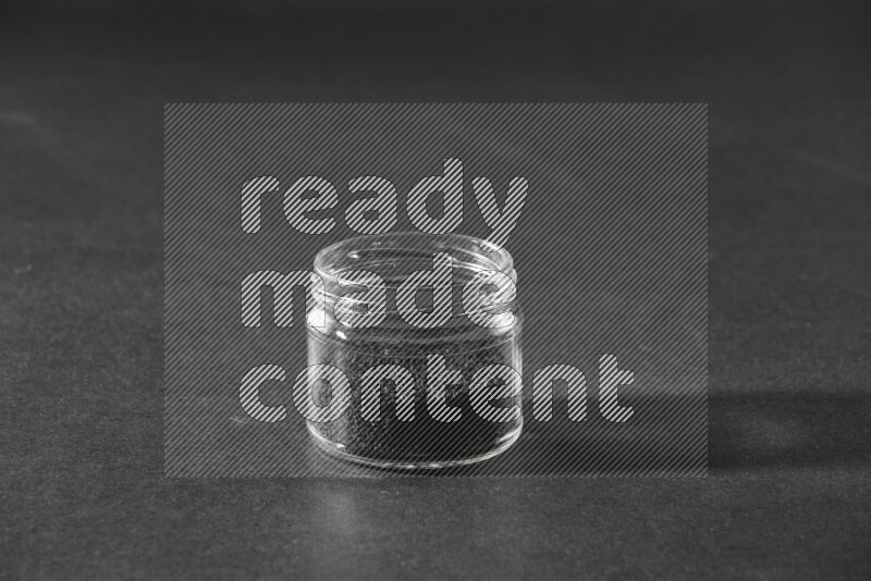 A glass jar full of black seeds on a black flooring