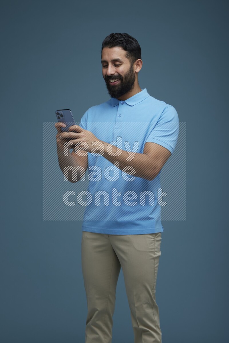 A man Texting on his phone in a blue background wearing a Blue shirt