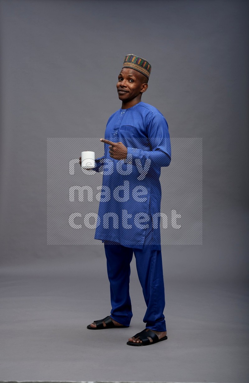 Man wearing Nigerian outfit standing holding mug on gray background