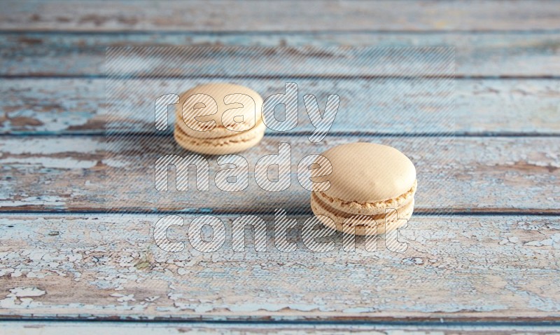 45º Shot of two White Caramel fleur de sel macarons on a light blue wooden background