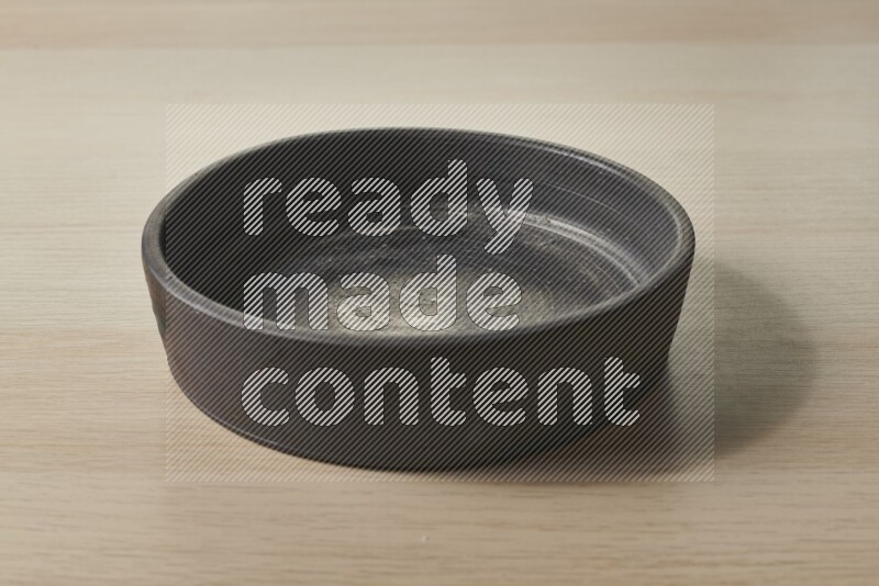 A black pottery oven plate on light wooden background