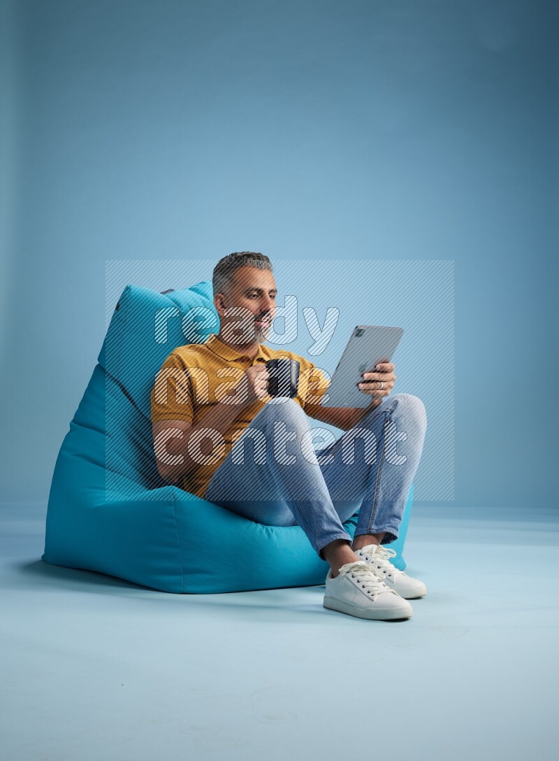 A man sitting on a blue beanbag and drinking coffee