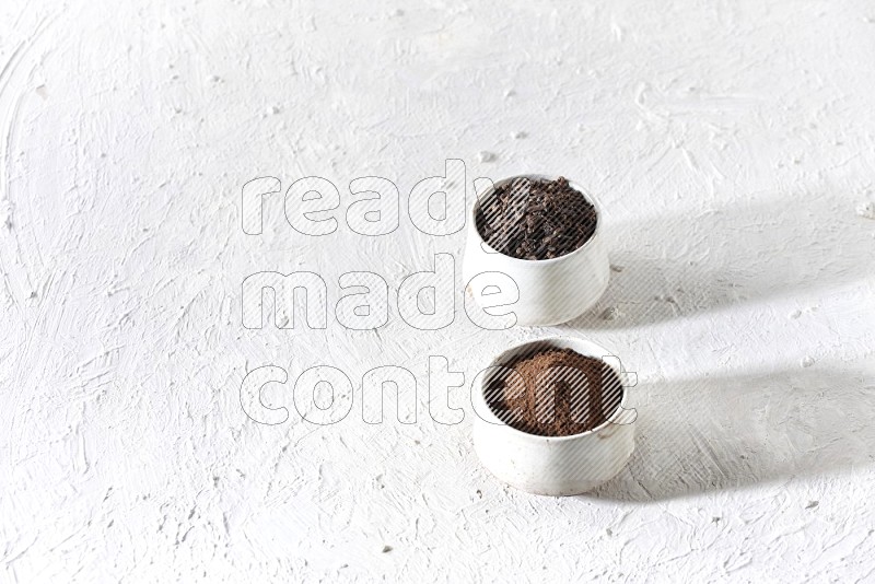 2 Beige ceramic bowls, one full of cloves and the other full of powder on textured white flooring