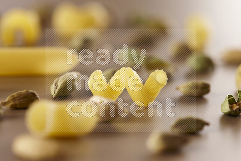 Raw pasta with different ingredients such as cherry tomatoes, garlic, onions, red chilis, black pepper, white pepper, bay laurel leaves, rosemary and cardamom on beige background