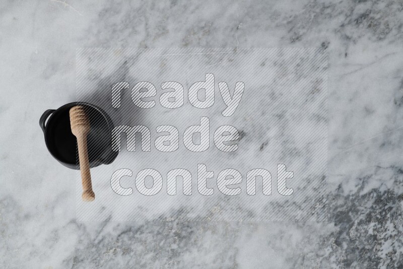 Black pottery bowl with wooden honey dipper in it on grey marble background