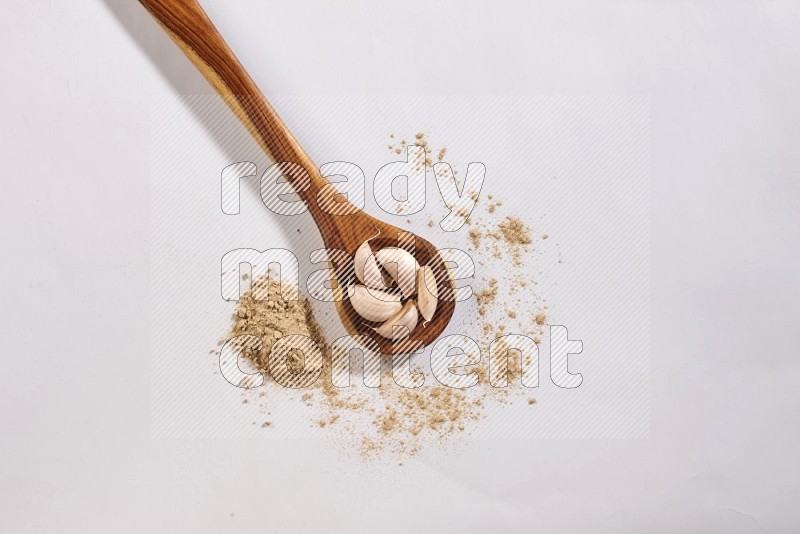 A wooden ladle full of garlic cloves with sprinkled powder on a white flooring