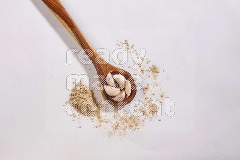 A wooden ladle full of garlic cloves on a white flooring in different angles