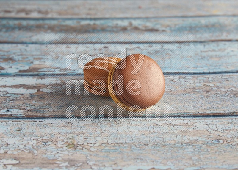 45º Shot of of two assorted Brown Irish Cream, and Yellow, and Brown Chai Latte macarons  on light blue background