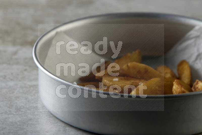 wedges potato on parchment paper in a stainless steel round tray on grey textured counter top