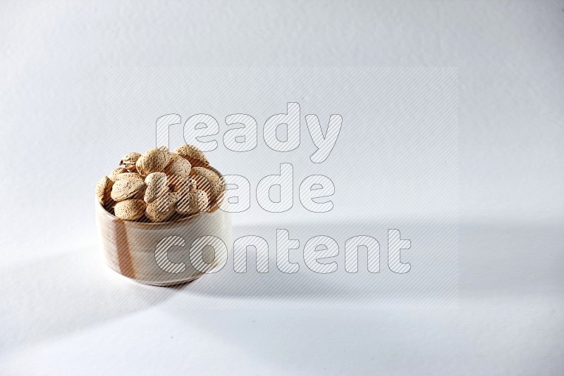 A beige ceramic bowl full of almonds on a white background in different angles