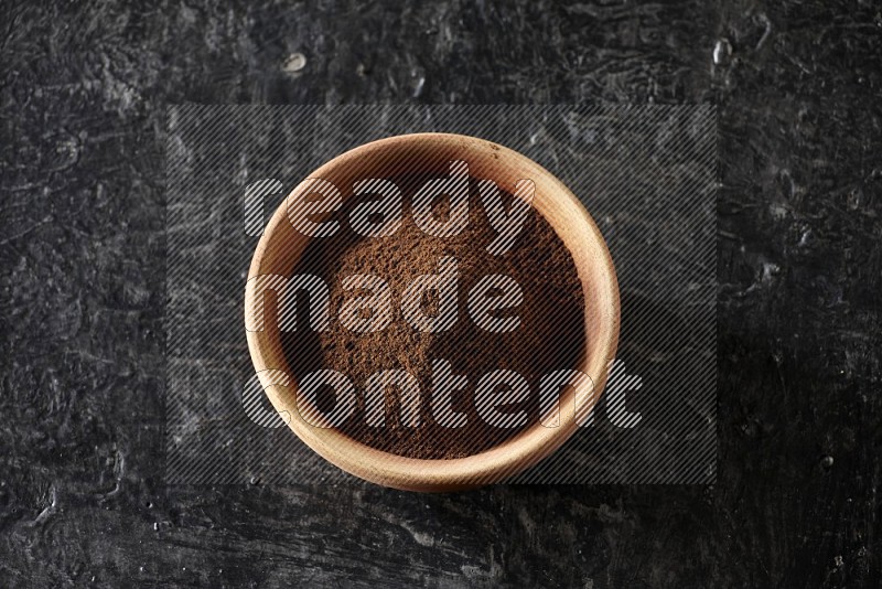 A wooden bowl full of cloves powder on a textured black flooring