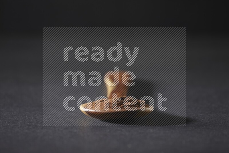 A wooden ladle full of cloves powder on a black flooring