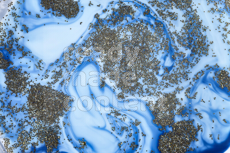 A close-up of sparkling gold glitter scattered on swirling blue background