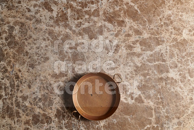 Top View Shot Of A Small Copper pan On beige Marble Flooring