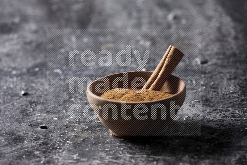بودرة القرفة في وعاء خشبي مع عود من القرفة على خلفية سوداء