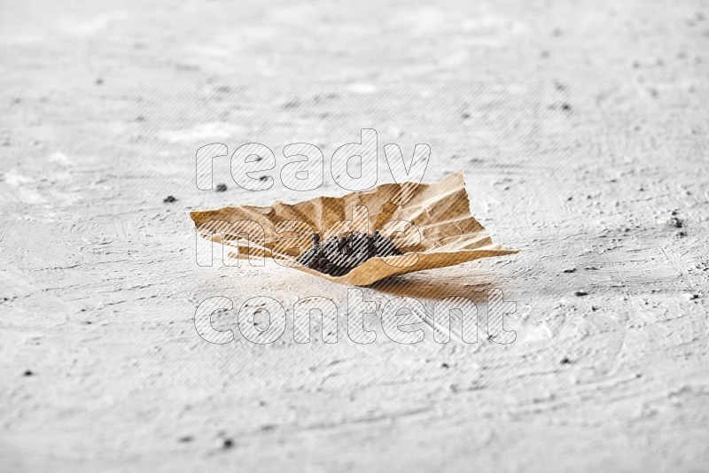 Black pepper on a crumpled paper on a textured white flooring