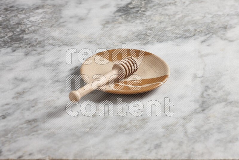 Multicolored pottery plate with wooden honey dipper in it on grey marble background