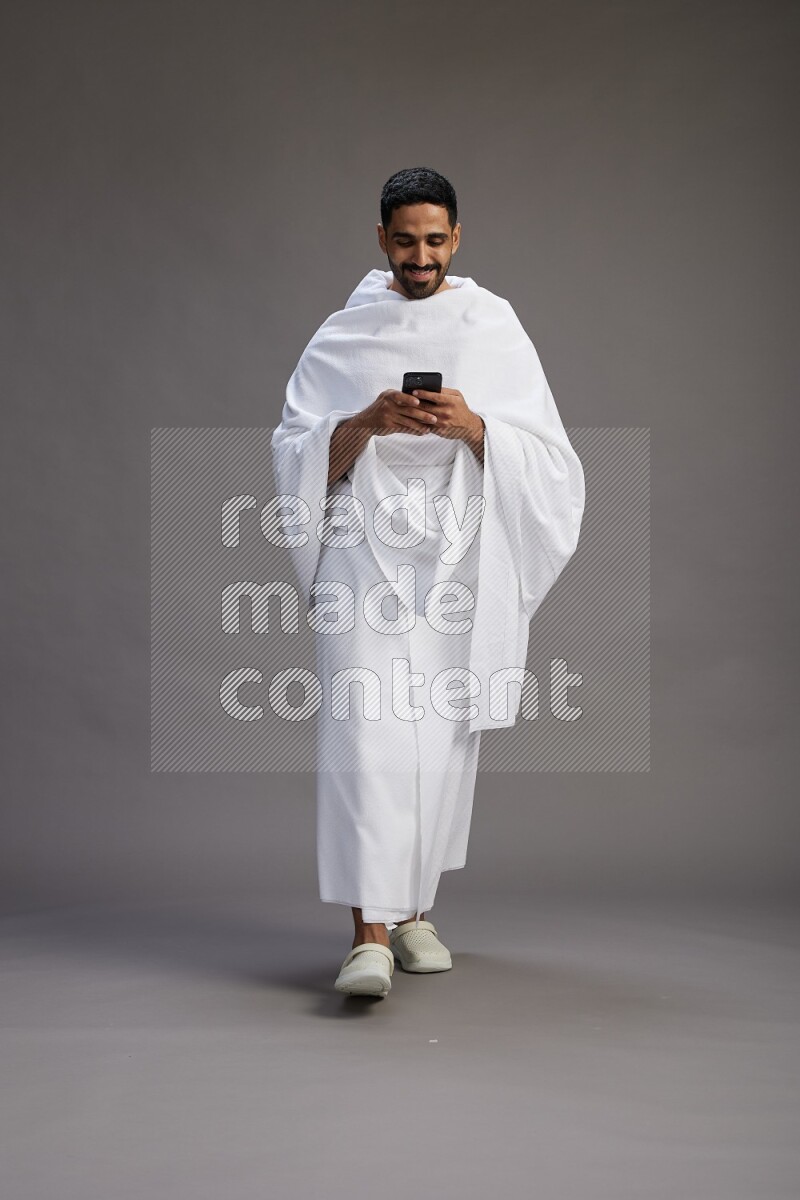 A man wearing Ehram Standing texting on phone on gray background