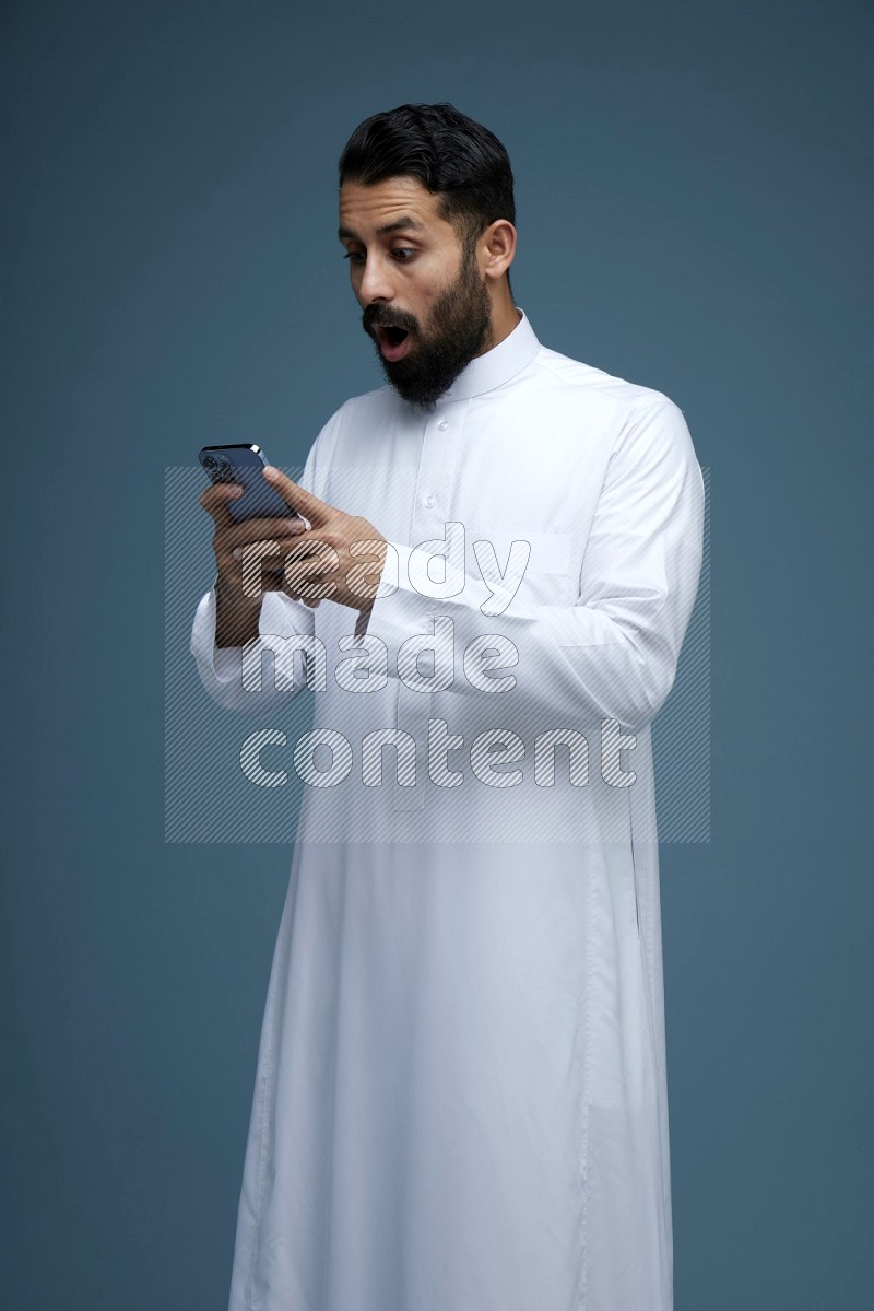 A man Texting in a blue background wearing Saudi Thob