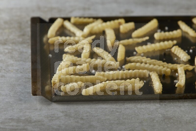 crinkle fries in a black stainless steel rectangle tray on grey textured counter top