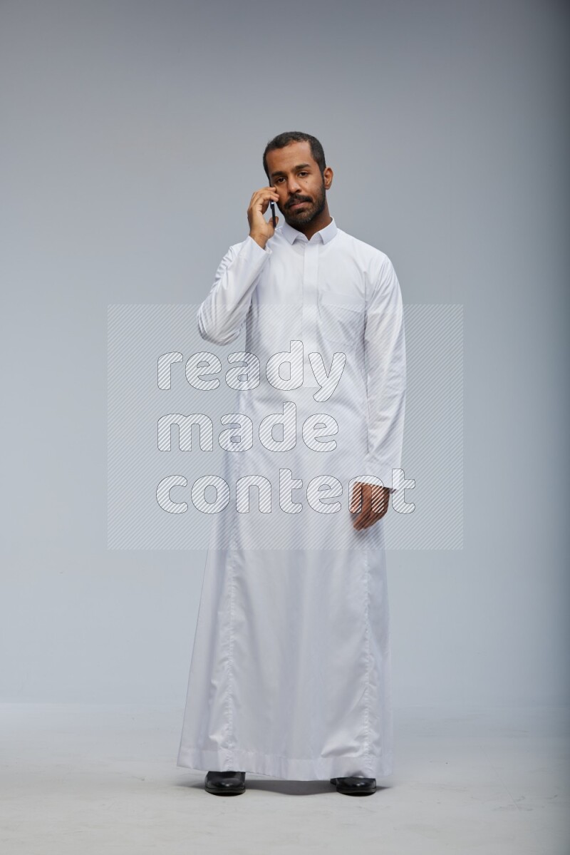 Saudi man wearing Thob standing talking on phone on Gray background