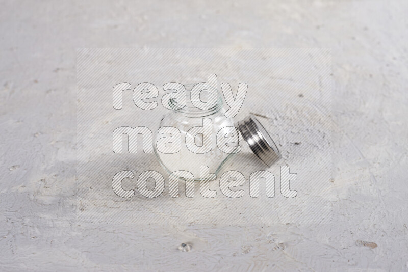 A glass jar full of coarse sea salt crystals on white background